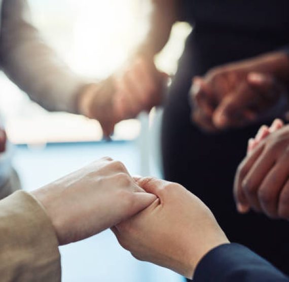 Cropped shot of a group of businesspeople standing together and holding hands in a modern office